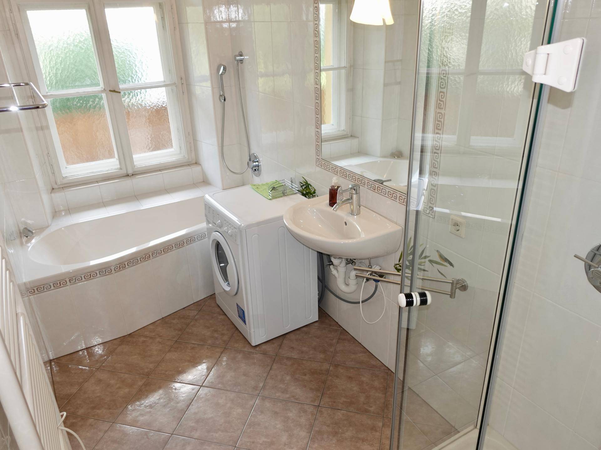 Badezimmer mit Badewanne, Duschkabine, Waschbecken und Fliesenboden, inklusive Waschmaschine.