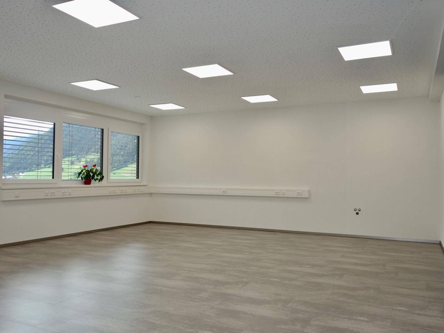 Geräumiger, leerer Büroraum mit großen Fenstern, die einen weiten Blick ins Grüne bieten.