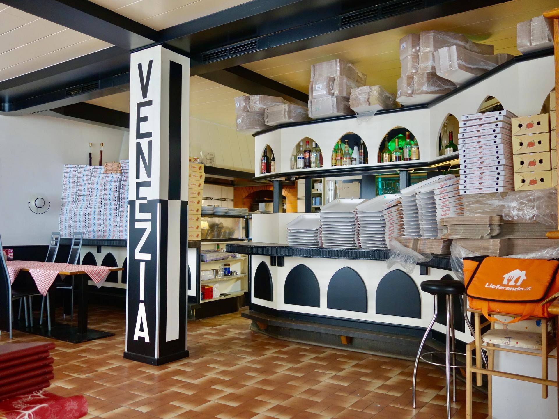 Innenansicht eines Restaurants mit Theke, Sitzgelegenheiten und vielen Pizzakartons.