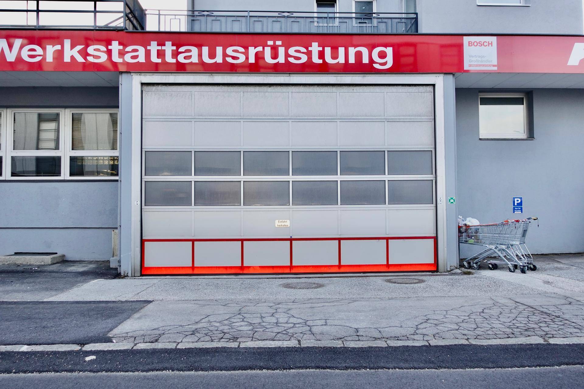 Großes Sektionaltor einer Werkstatt oder Lagerhalle mit Fenstersegmenten und roter Markierung.