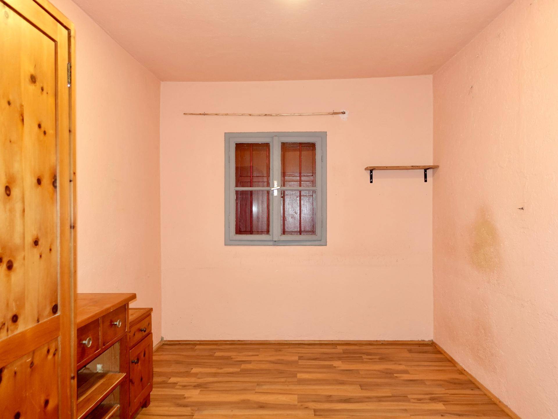 Schlichtes Schlafzimmer mit Holzschrank, Laminatboden und einem Fenster.