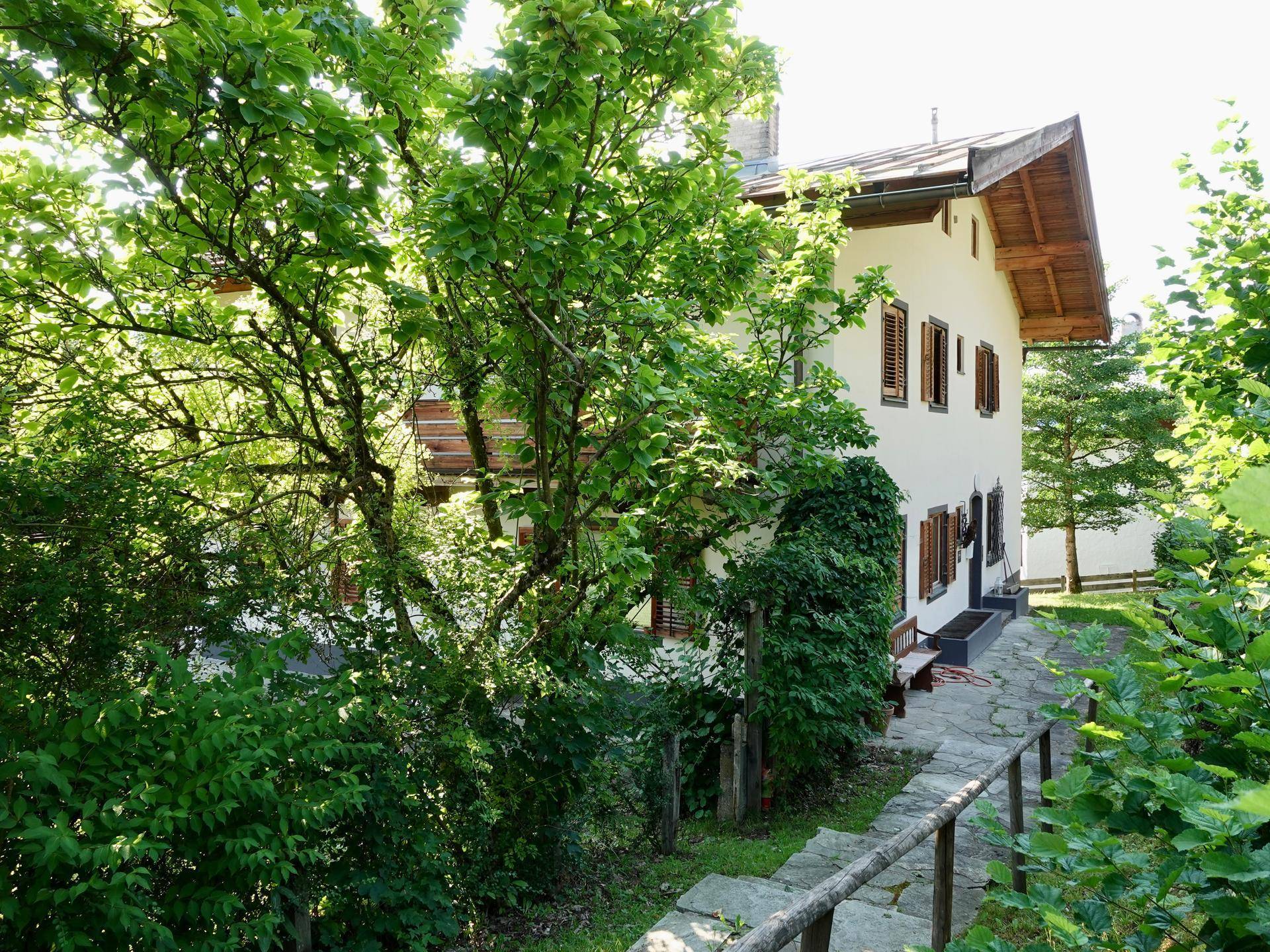 Traditionelles Haus mit Holzbalkonen, umgeben von üppigem Grün und einem Steinweg.