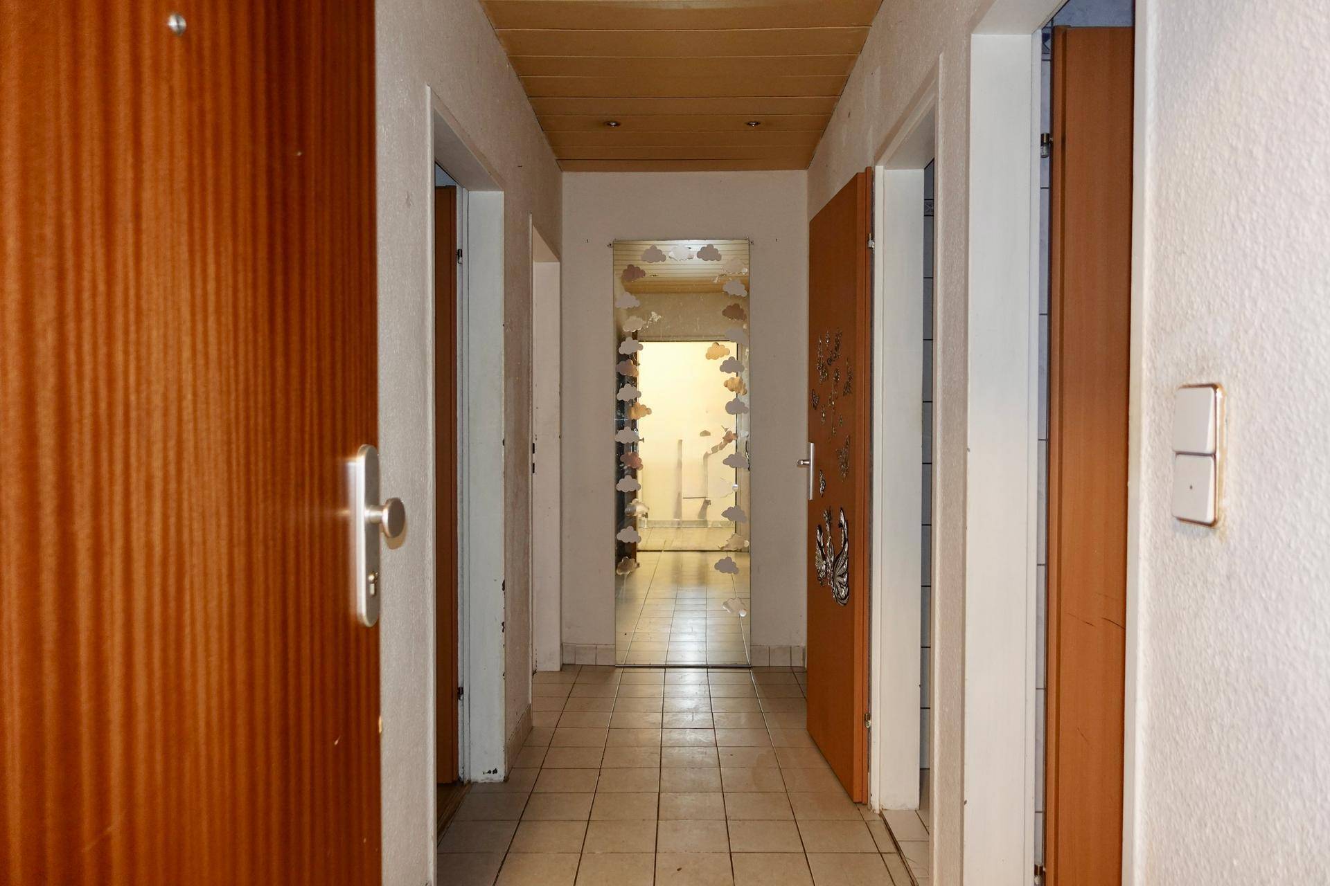 Langer Flur mit Fliesenboden und mehreren Holztüren, der zu weiteren Räumen führt.
