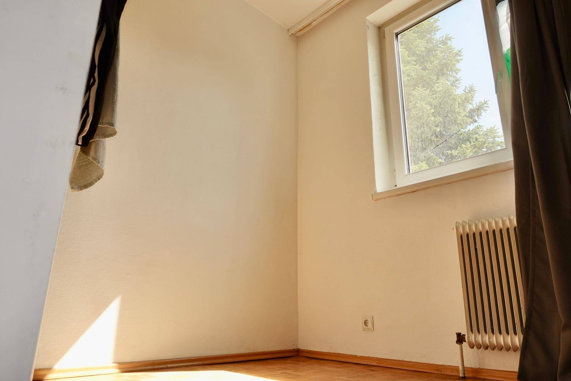 Helle Raumecke mit Fenster, Heizkörper und Parkettboden, gut beleuchtet.