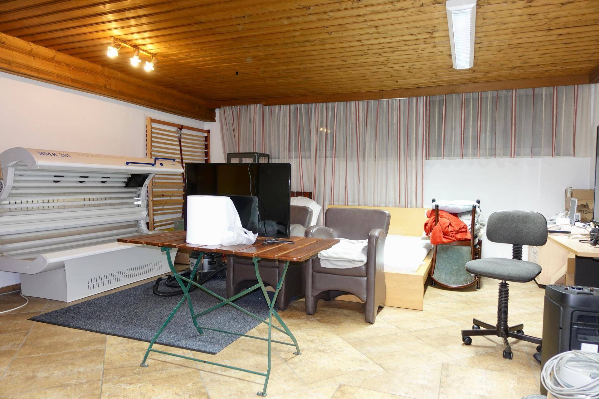 Ein vielseitiger Raum mit Holzdecke, einem Solarium, Sitzgelegenheiten und einem Arbeitstisch, der verschiedene Nutzungen ermöglicht.