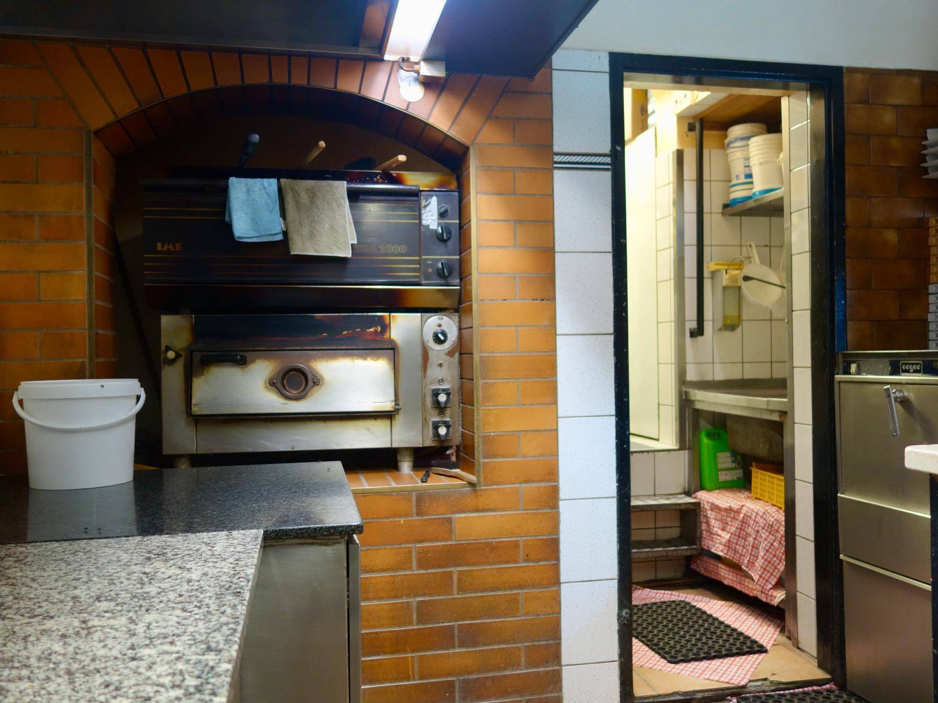 Professionelle Küche mit einem großen gemauerten Pizzaofen und Arbeitsflächen aus Granit.