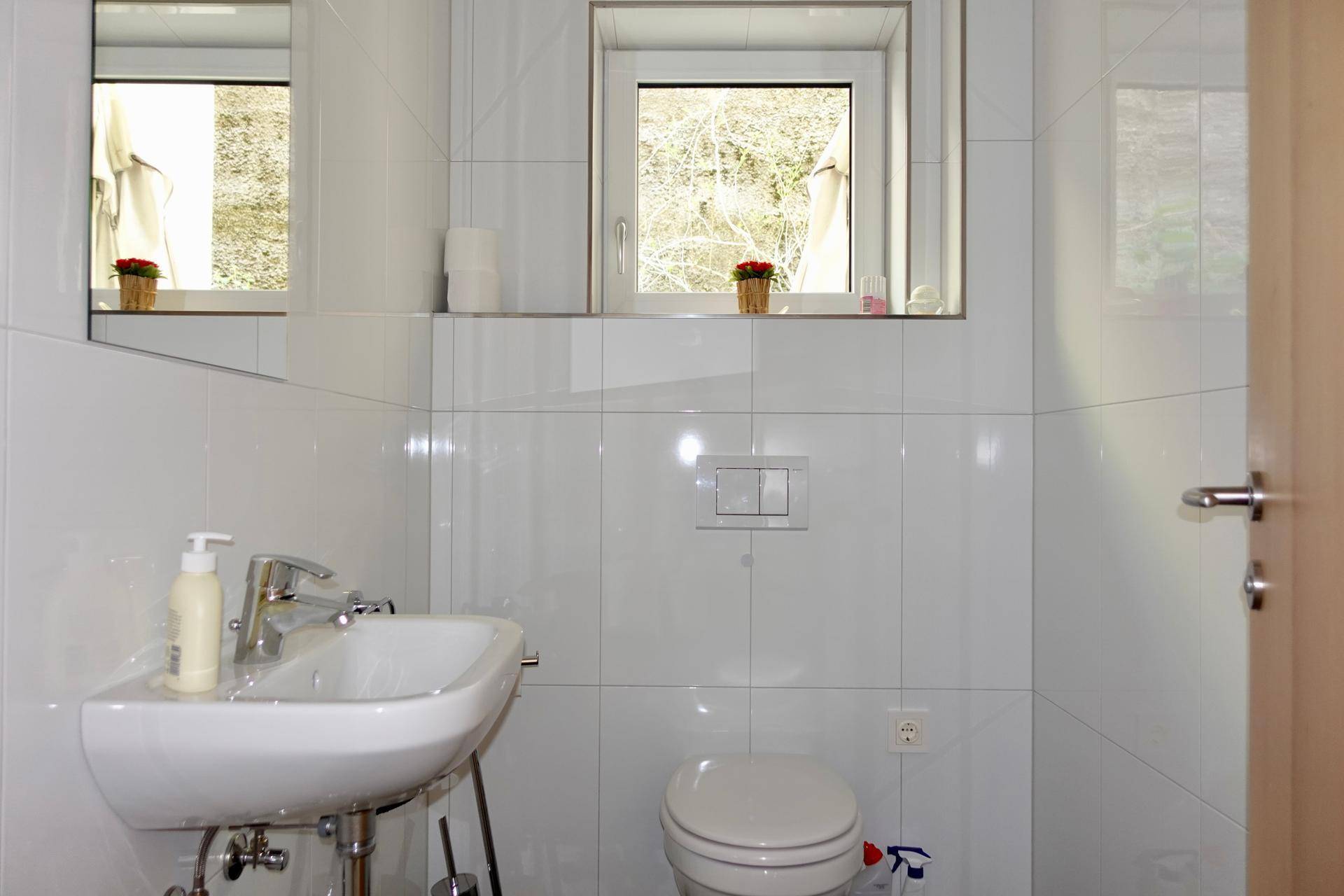 Kleines Gäste-WC mit Fenster, Waschbecken und Wand-WC.