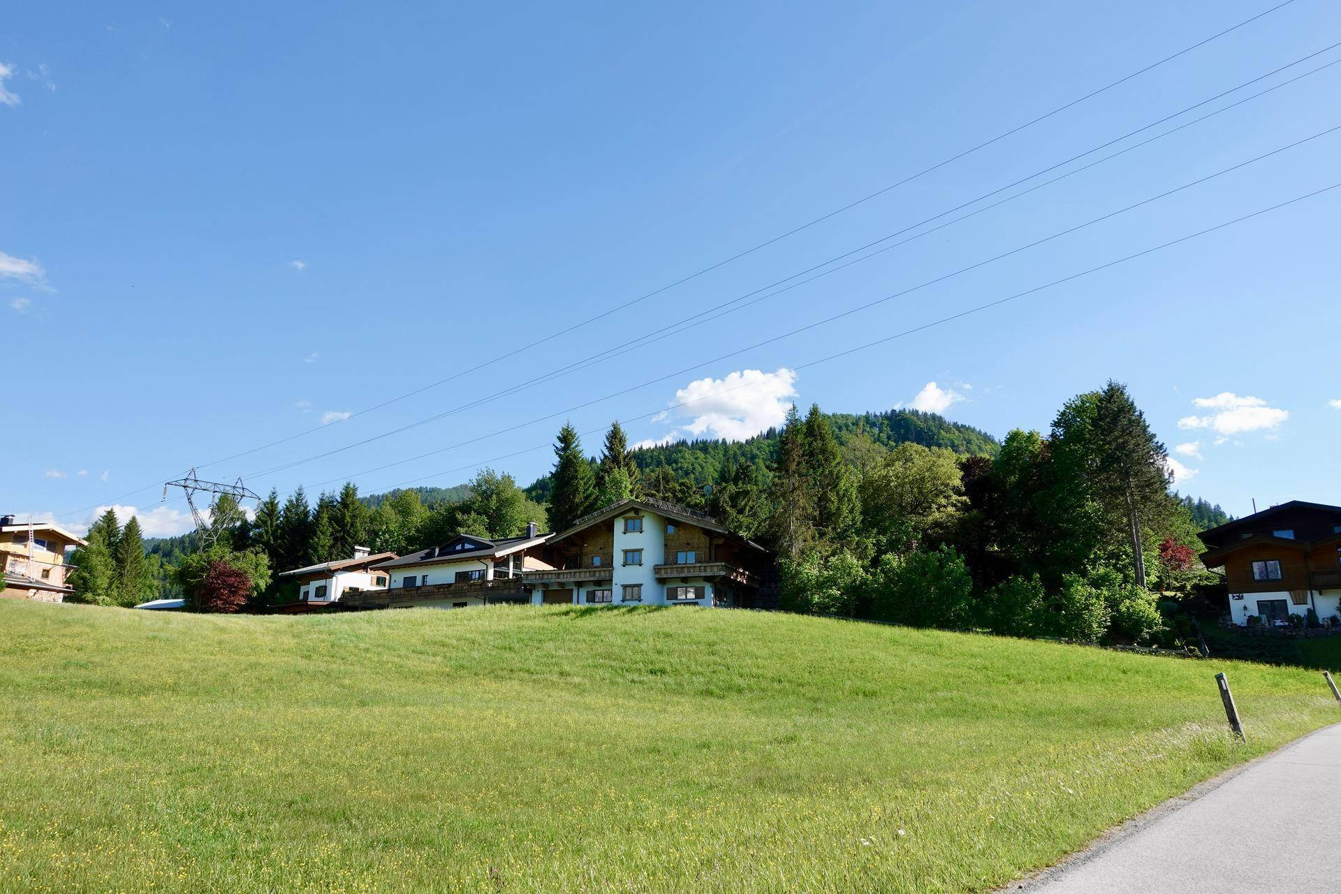 Weitläufige grüne Wiesen mit Häusern im Hintergrund unter blauem Himmel.