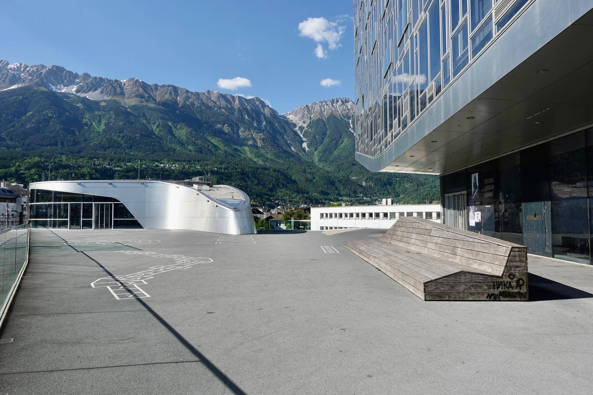 Moderne Architektur mit Glasfassaden und einer Holzbank vor einer beeindruckenden Bergkulisse.