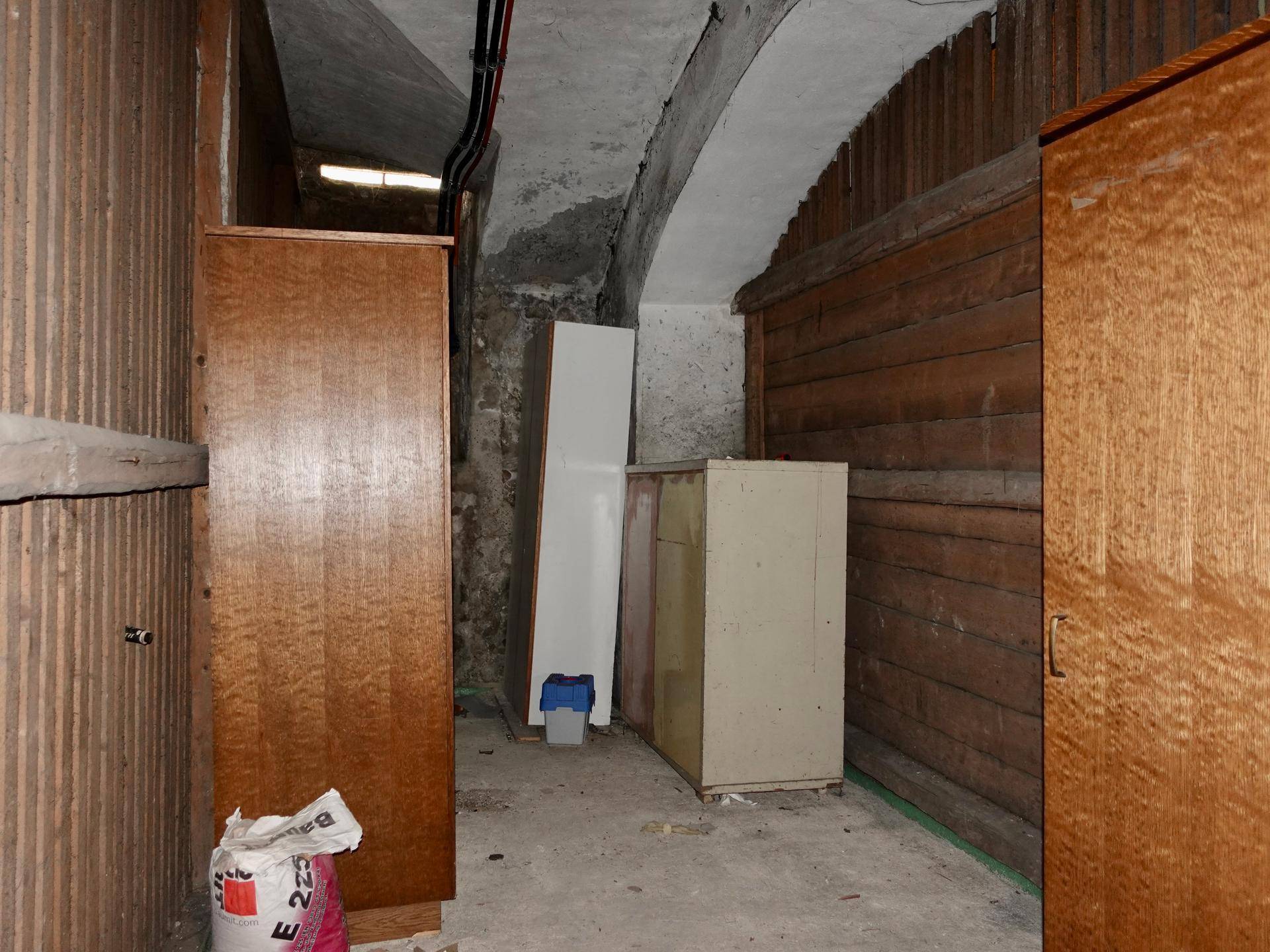Kellerraum mit Holzwänden, Betonboden und Lagerflächen unter einem sichtbaren Gewölbe.