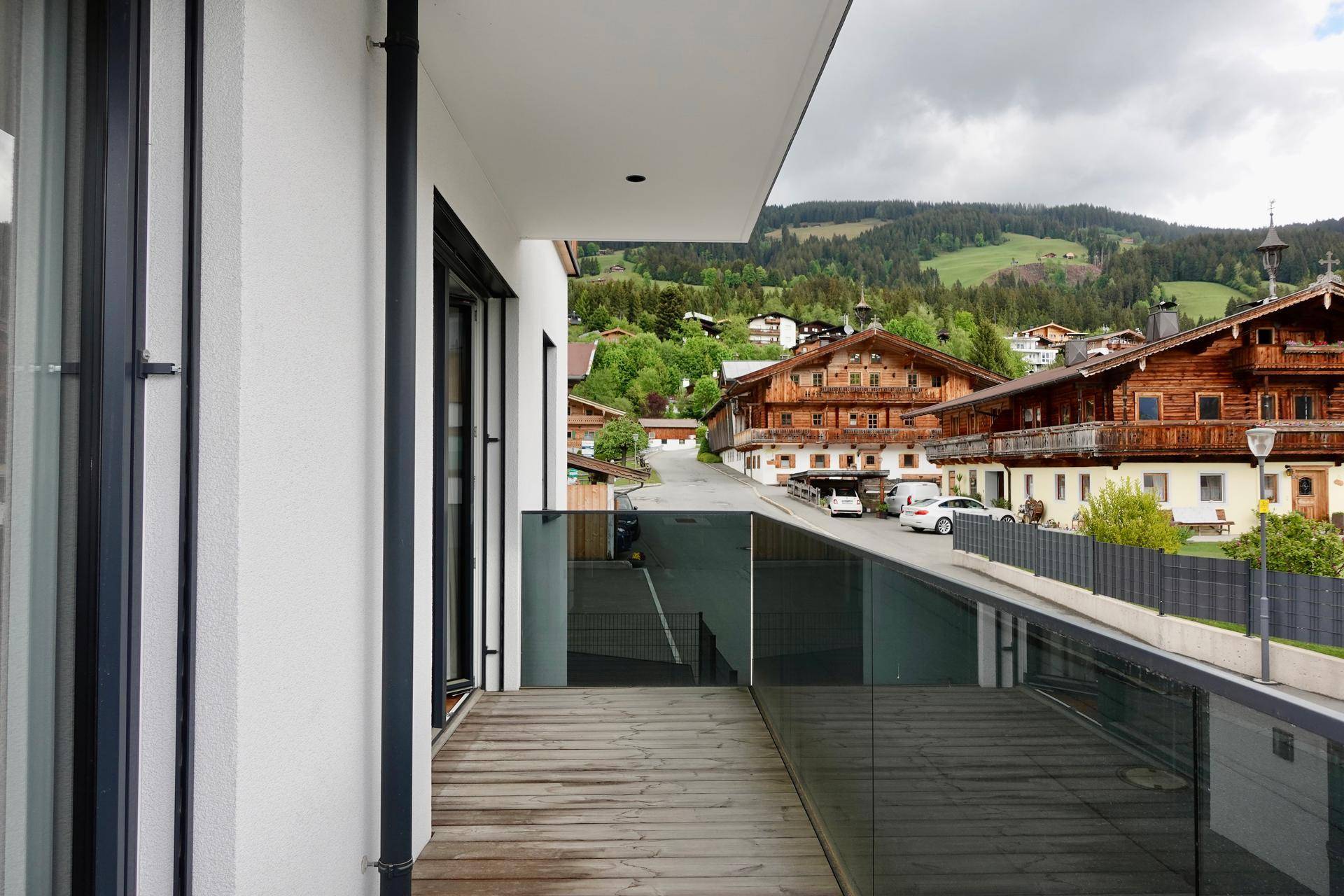 Geräumiger Balkon mit Holzboden, Glasbrüstung und Blick auf die umliegende Berglandschaft.