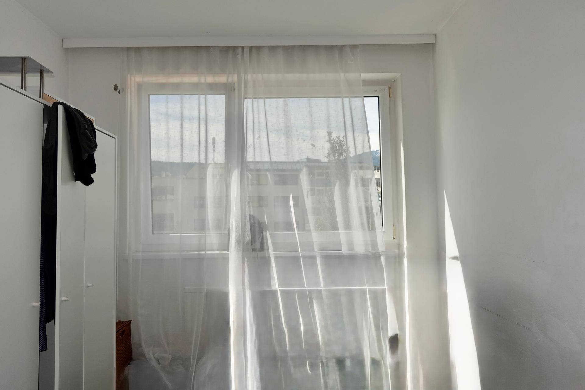 Heller Raum mit großem Fenster und transparenten weißen Vorhängen, viel Tageslicht.