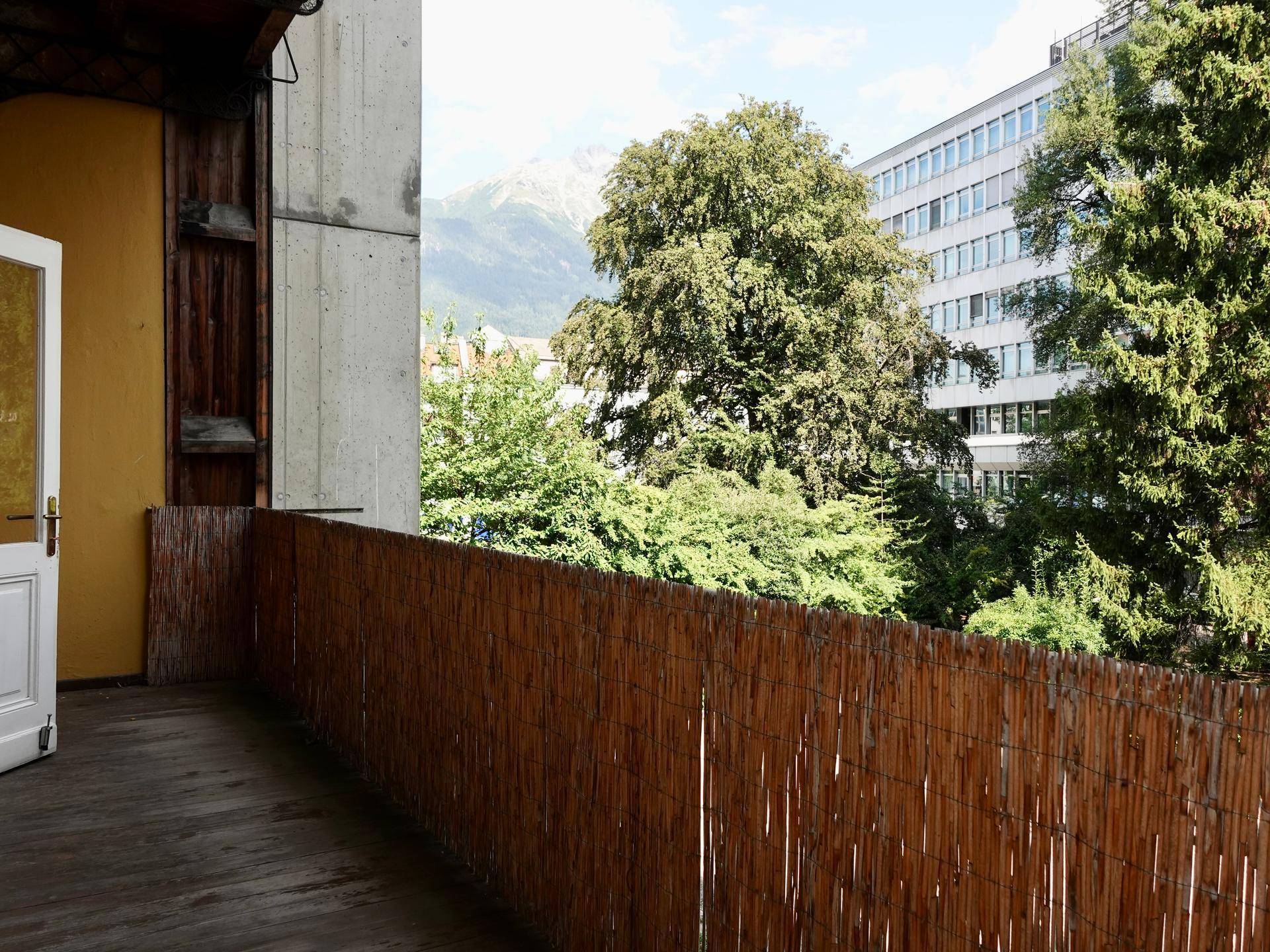 Balkon mit Holzboden, Bambusverkleidung und einem weiten Blick auf Bäume und Berge im Hintergrund.