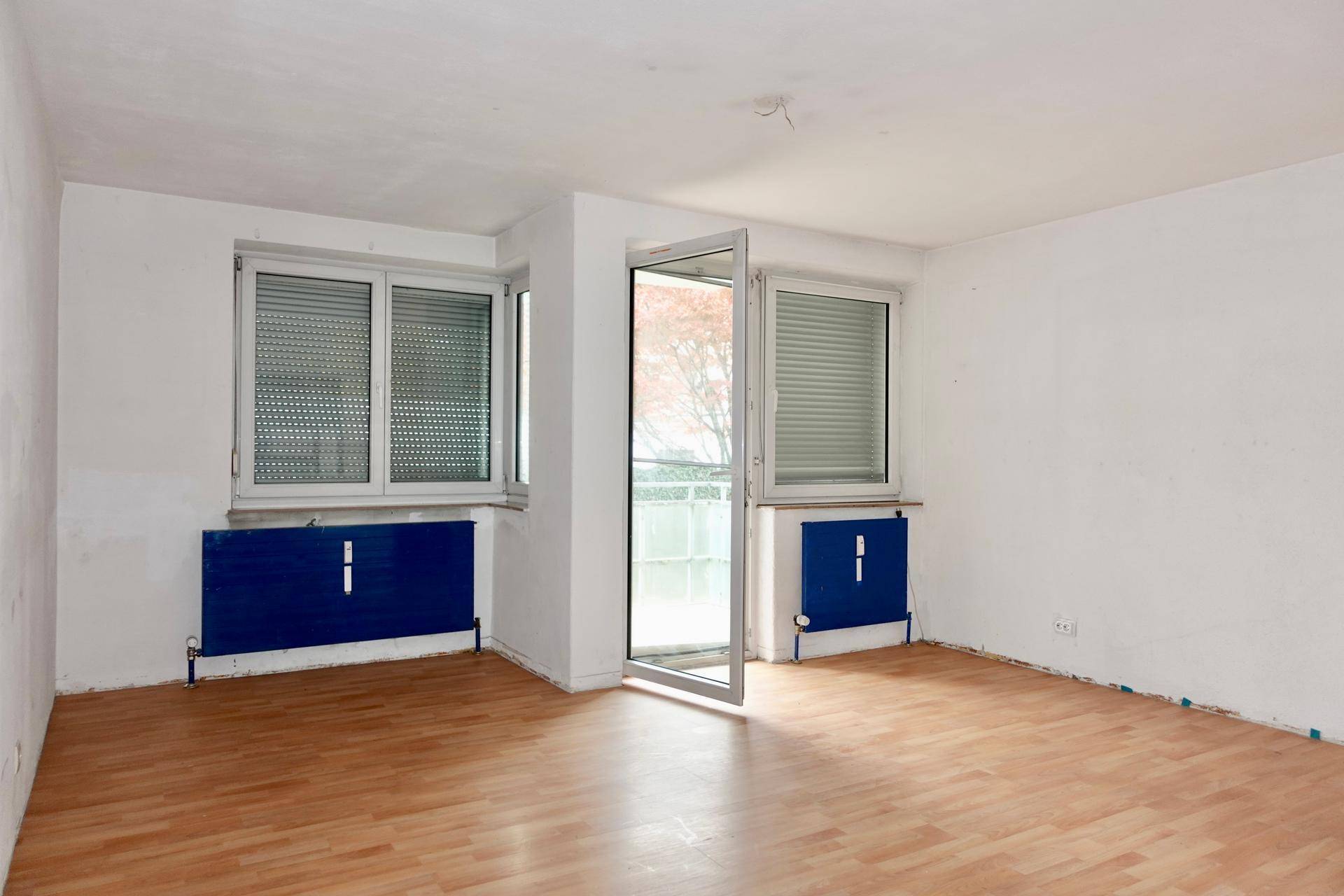 Heller Raum mit Laminatboden, zwei Fenstern und Zugang zu einem Balkon.