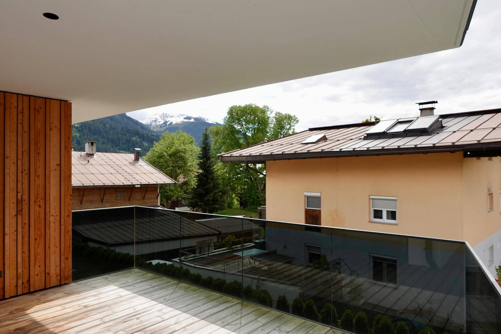 Geräumiger Balkon mit Holzboden, Glasbrüstung und beeindruckendem Bergblick.