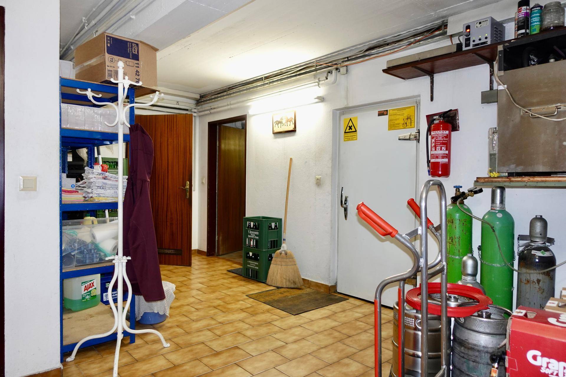 Ein Lagerraum mit Regalen, Gasflaschen und einem Feuerlöscher, der verschiedene Utensilien und Vorräte beherbergt.
