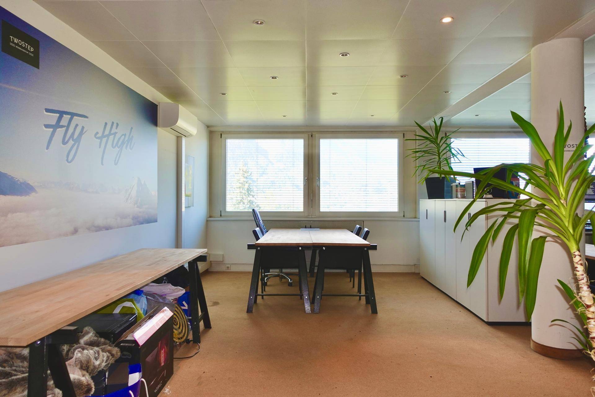 Modernes Büro mit Schreibtischen, Pflanzen und großen Fenstern mit Bergblick.
