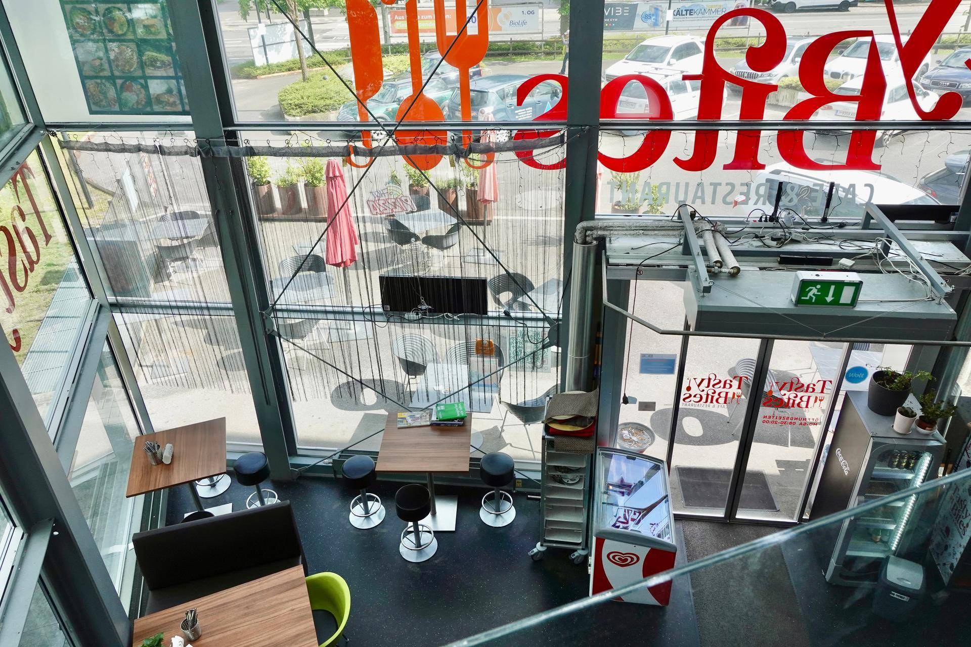 Blick von oben in ein modernes Restaurant mit hohen Fenstern und Blick auf den Außenbereich.