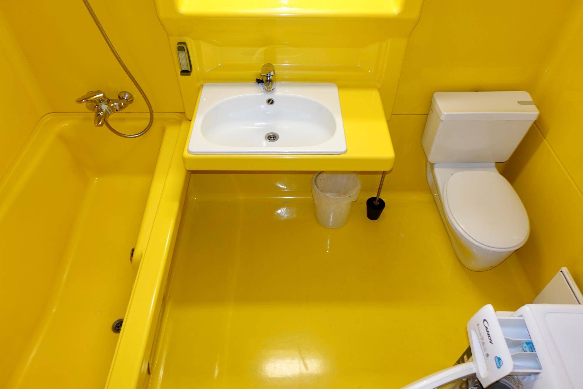 Ein kleines, hellgelbes Badezimmer mit Badewanne, Waschbecken und Toilette, das eine lebendige Farbe aufweist.