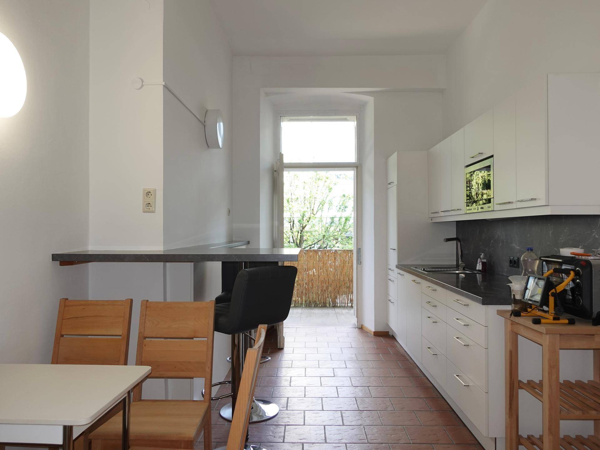 Moderne Küche mit weißen Schränken, Edelstahlspüle und Zugang zu einem Balkon, mit Fliesenboden.