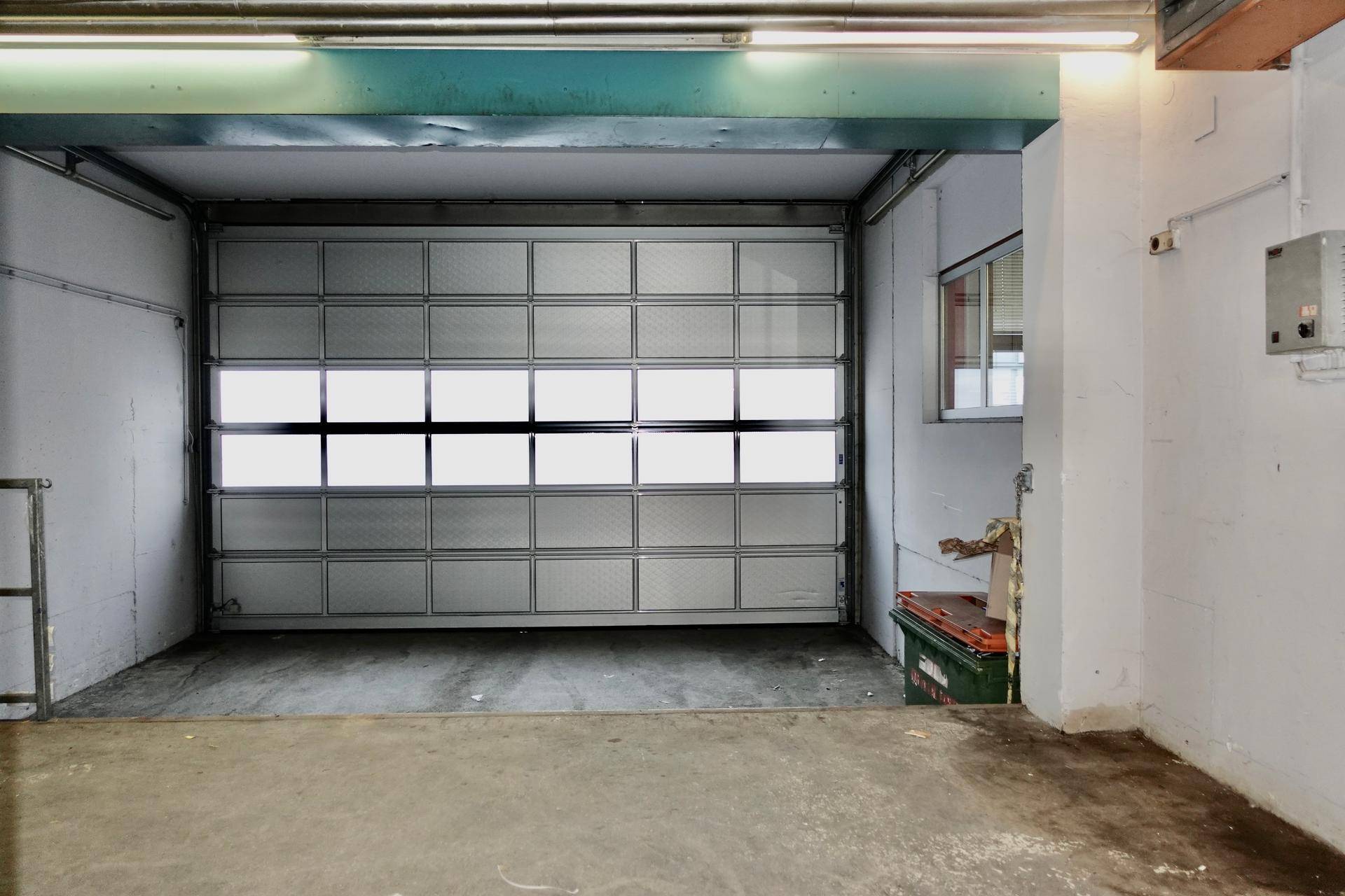 Innenansicht einer Garage mit Sektionaltor, Betonboden und einem kleinen Fenster.