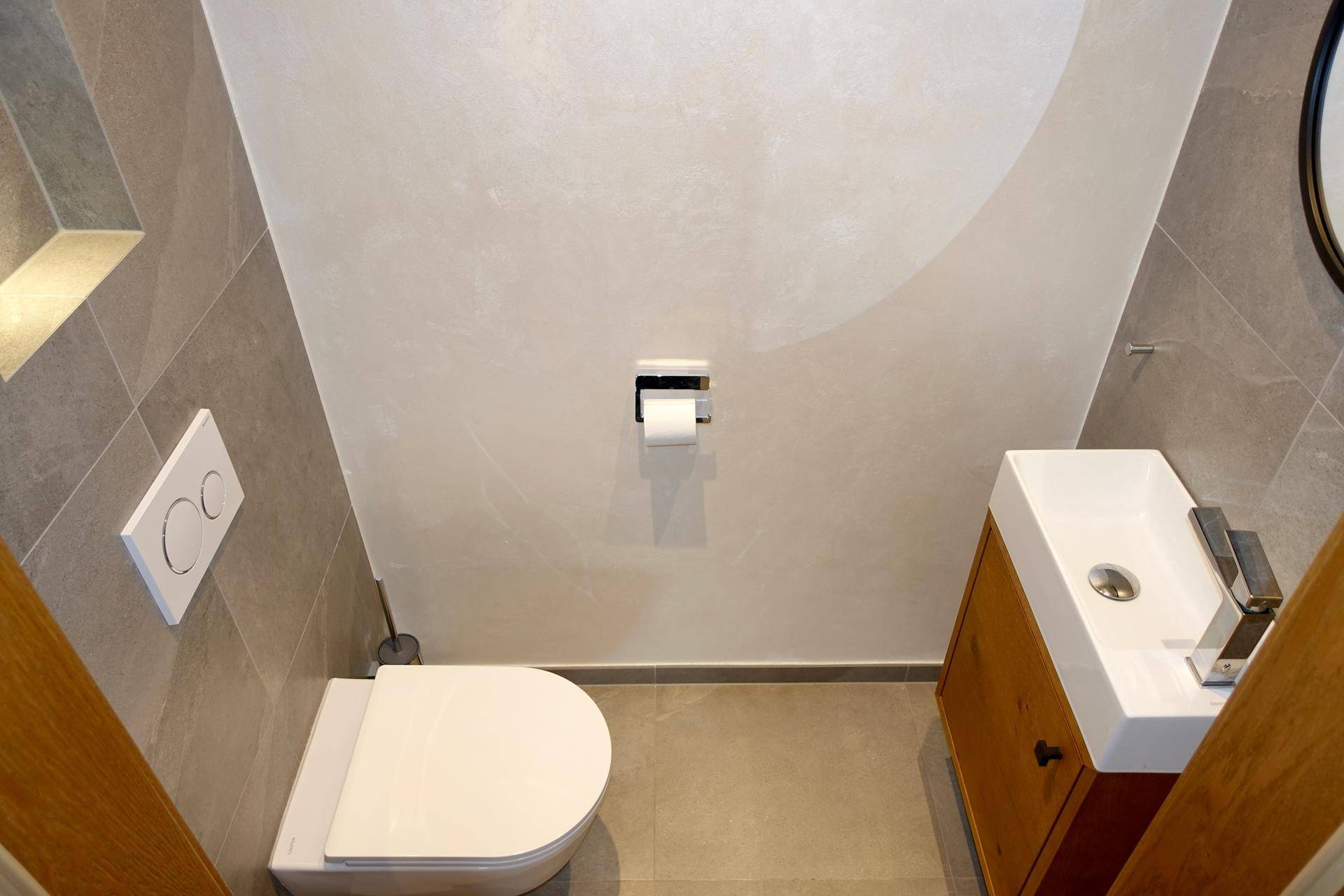 Modernes Gäste-WC mit Wand-WC, kleinem Waschbecken und grauen Fliesen.