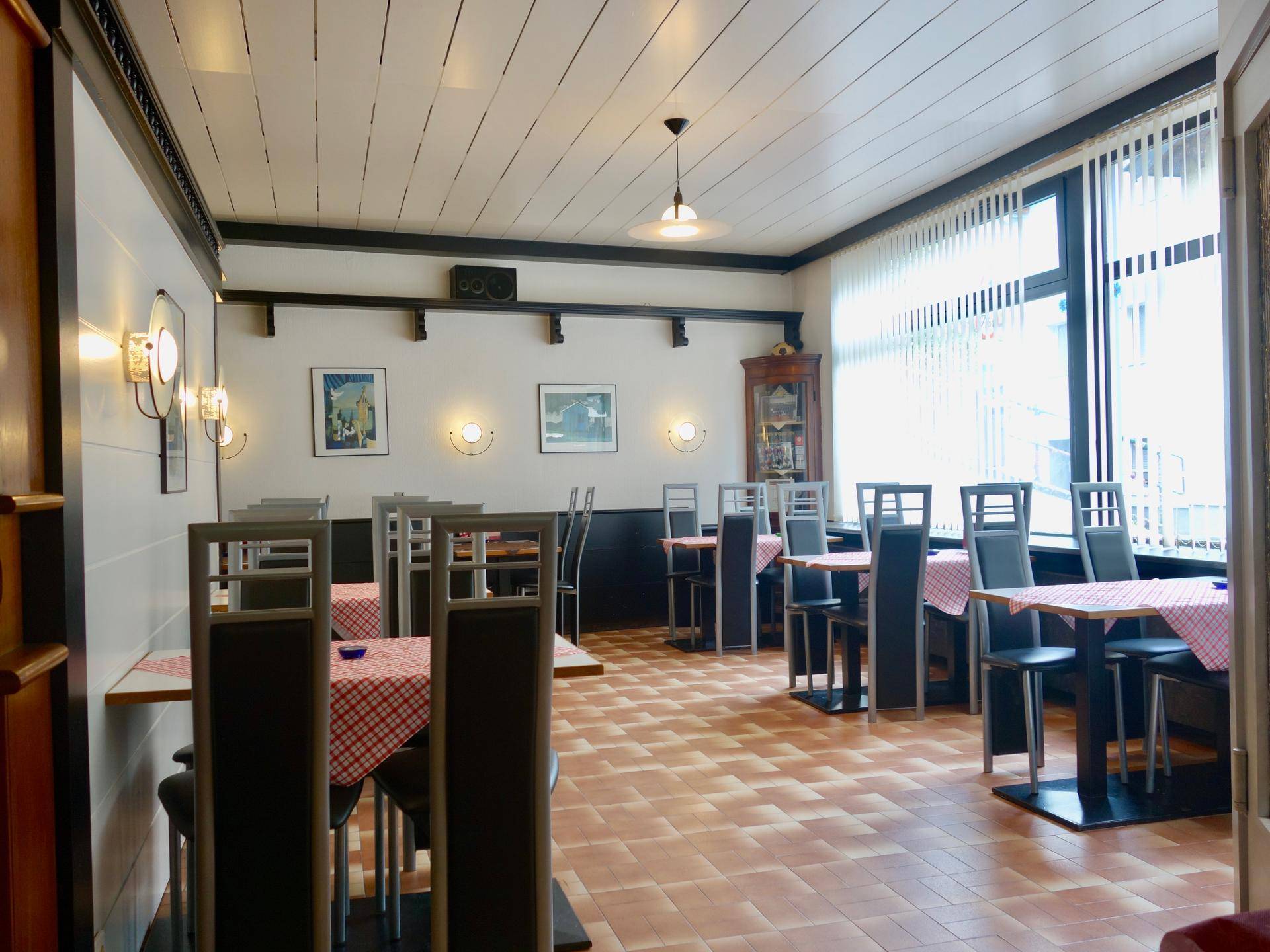 Geräumiger Restaurantbereich mit mehreren Tischen und Stühlen, Blick auf die Fenster mit Jalousien.
