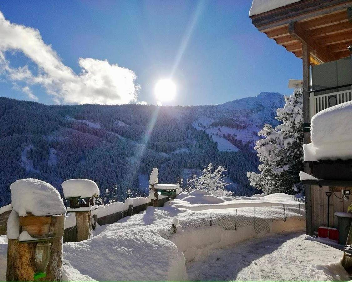 Winterliche Berglandschaft mit tief verschneiten Bäumen und einem Haus unter strahlendem Sonnenschein.