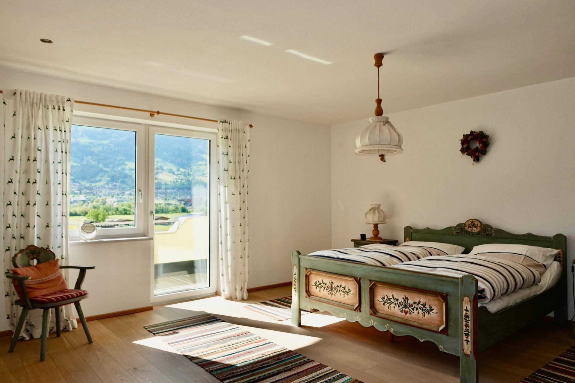 Helles Schlafzimmer mit traditionellem Bett, Holzboden und Bergblick.