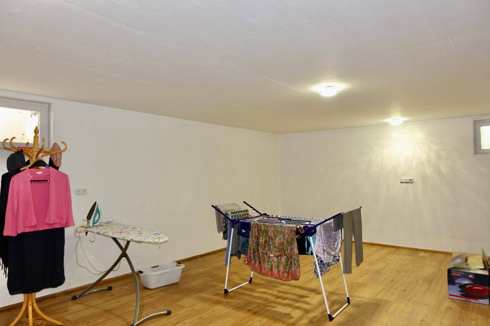 Ausgebauter Kellerraum mit Holzfußboden, Fenster und Platz für Wäschetrocknung.