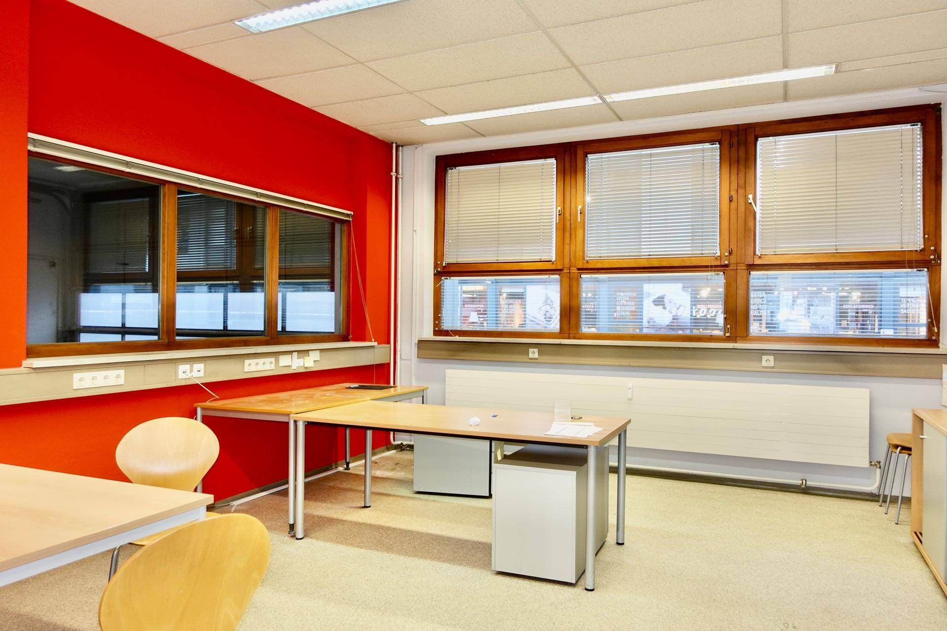 Büro mit leuchtend roten Wänden, Holzfenstern und Jalousien, ausgestattet mit Schreibtischen.