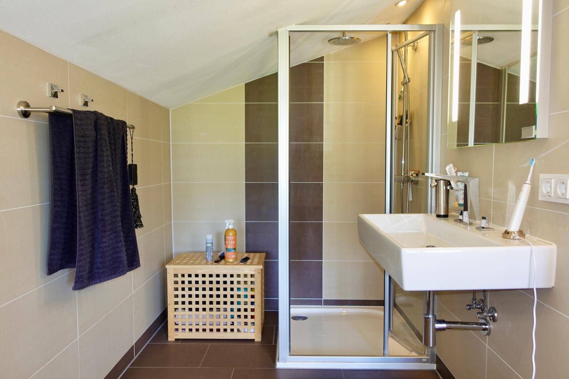 Modernes Badezimmer mit Dusche, Waschbecken und Dachschräge, hell gefliest.