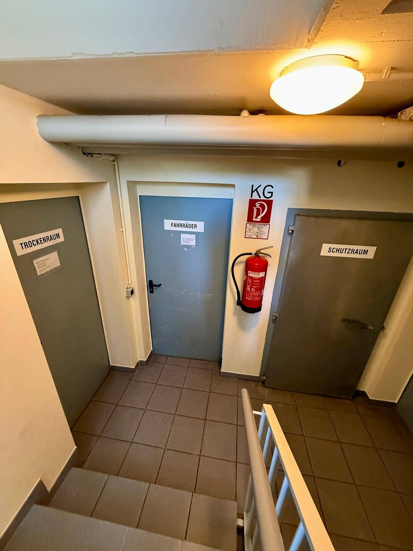 Kellerflur mit Zugang zu Trockenraum, Fahrradraum und Schutzraum, inklusive Feuerlöscher.