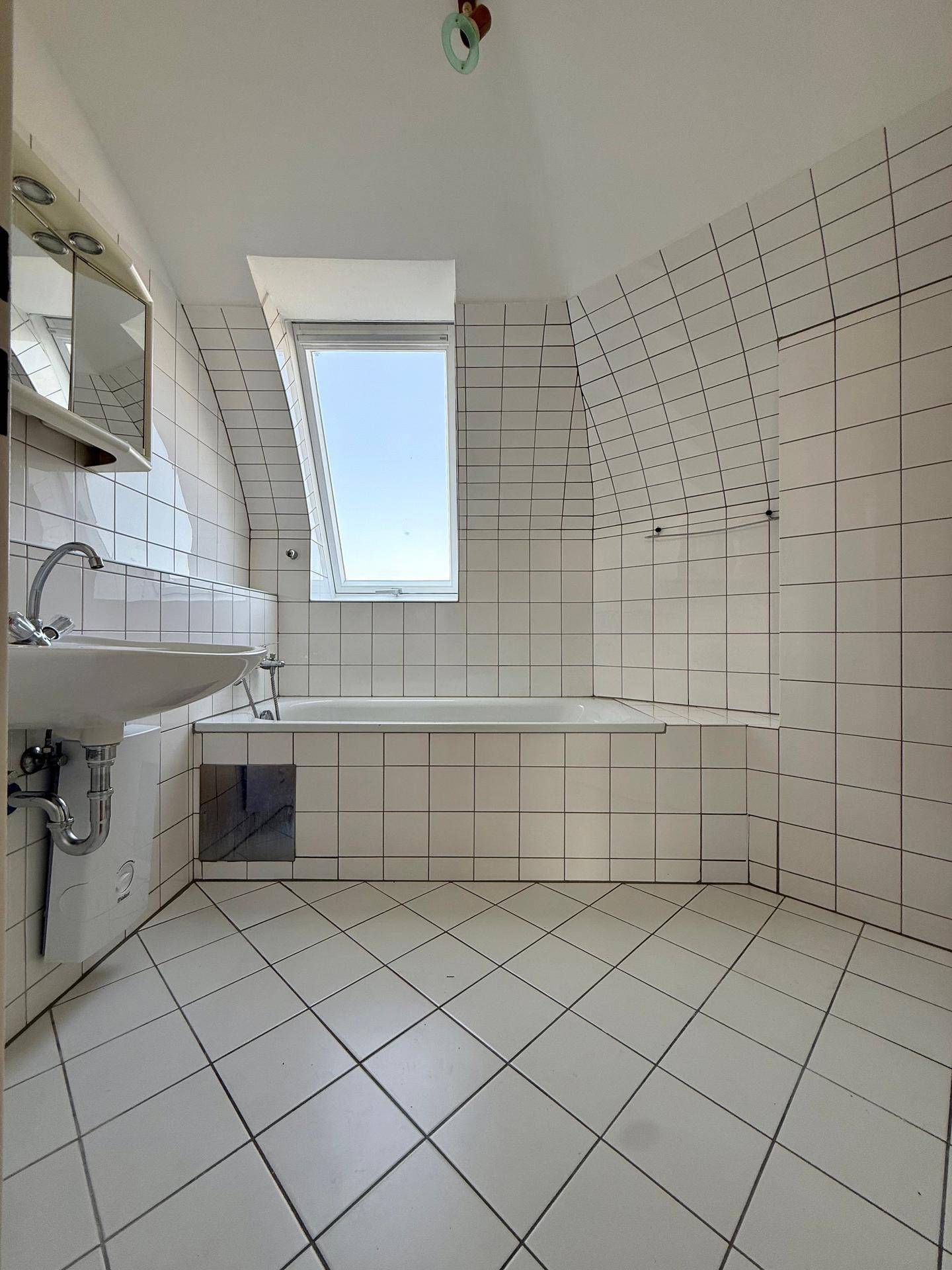 Badezimmer mit Badewanne, Waschbecken und Dachfenster, komplett gefliest in Weiß.