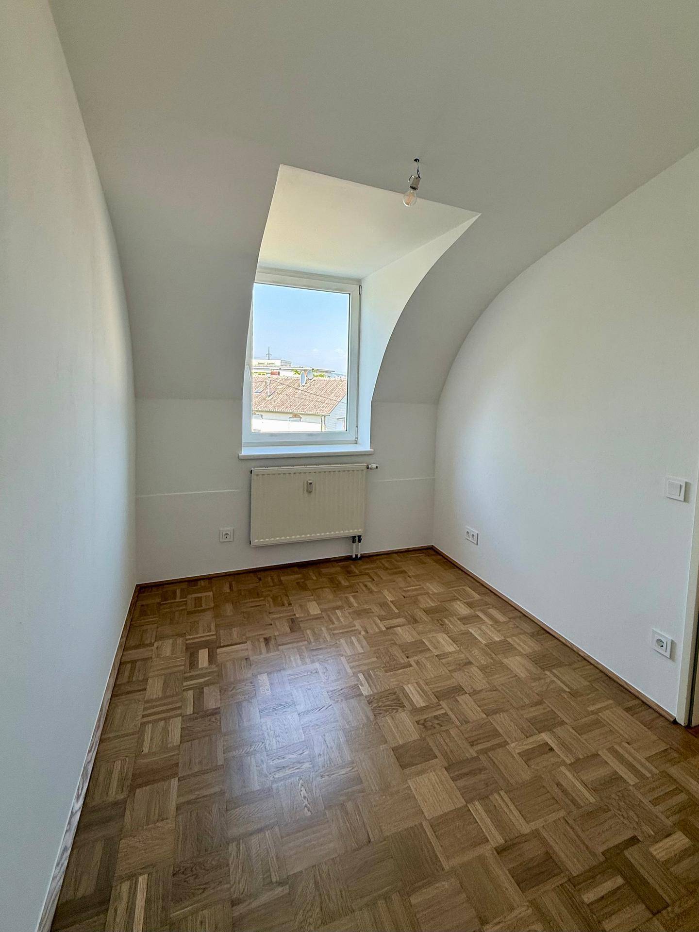 Helles Schlafzimmer mit Parkettboden, Dachschräge und Fenster, das eine angenehme Atmosphäre schafft.