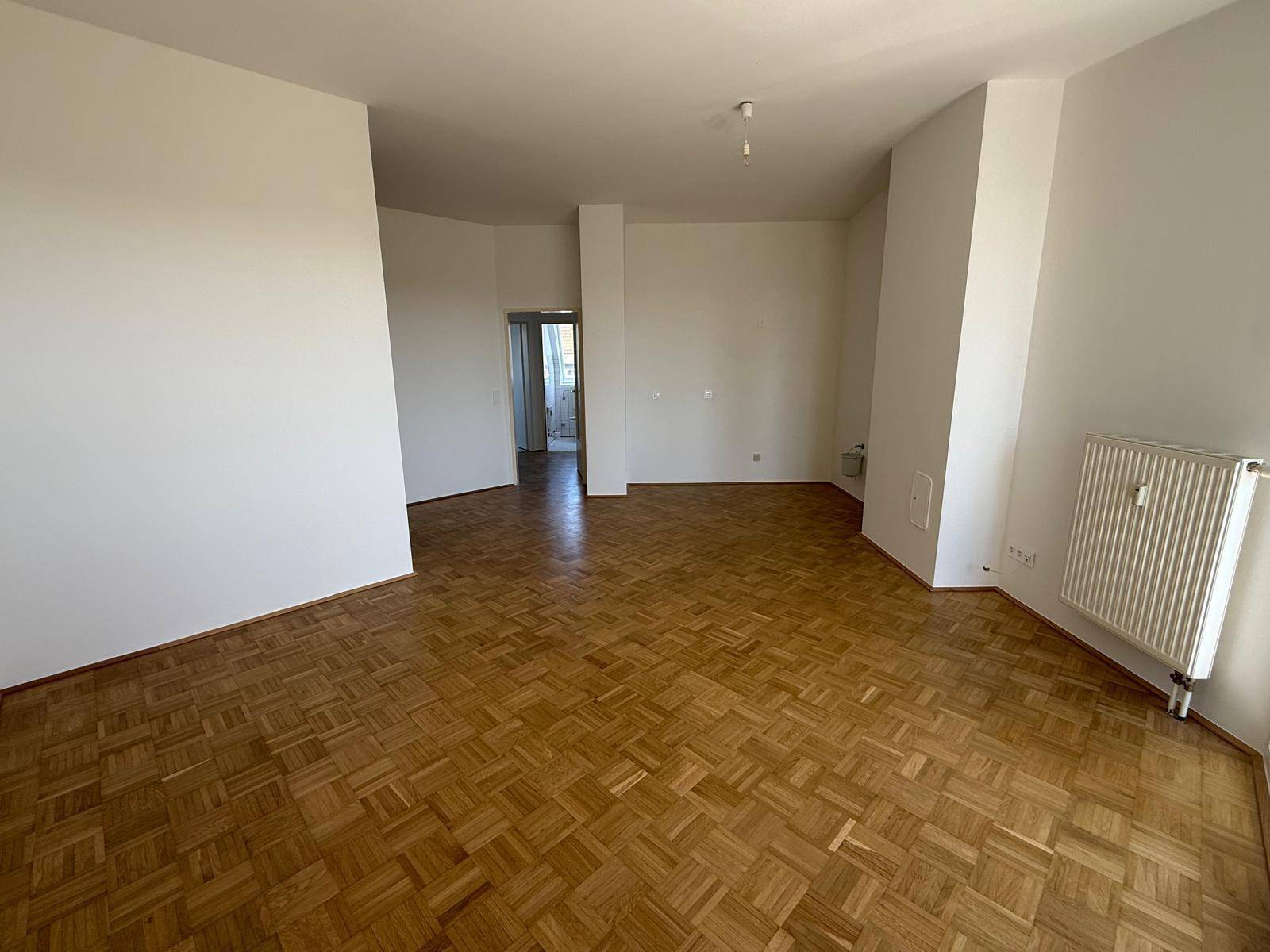 Großzügiges Wohnzimmer mit Parkettboden, das in einen weiteren Raum führt.
