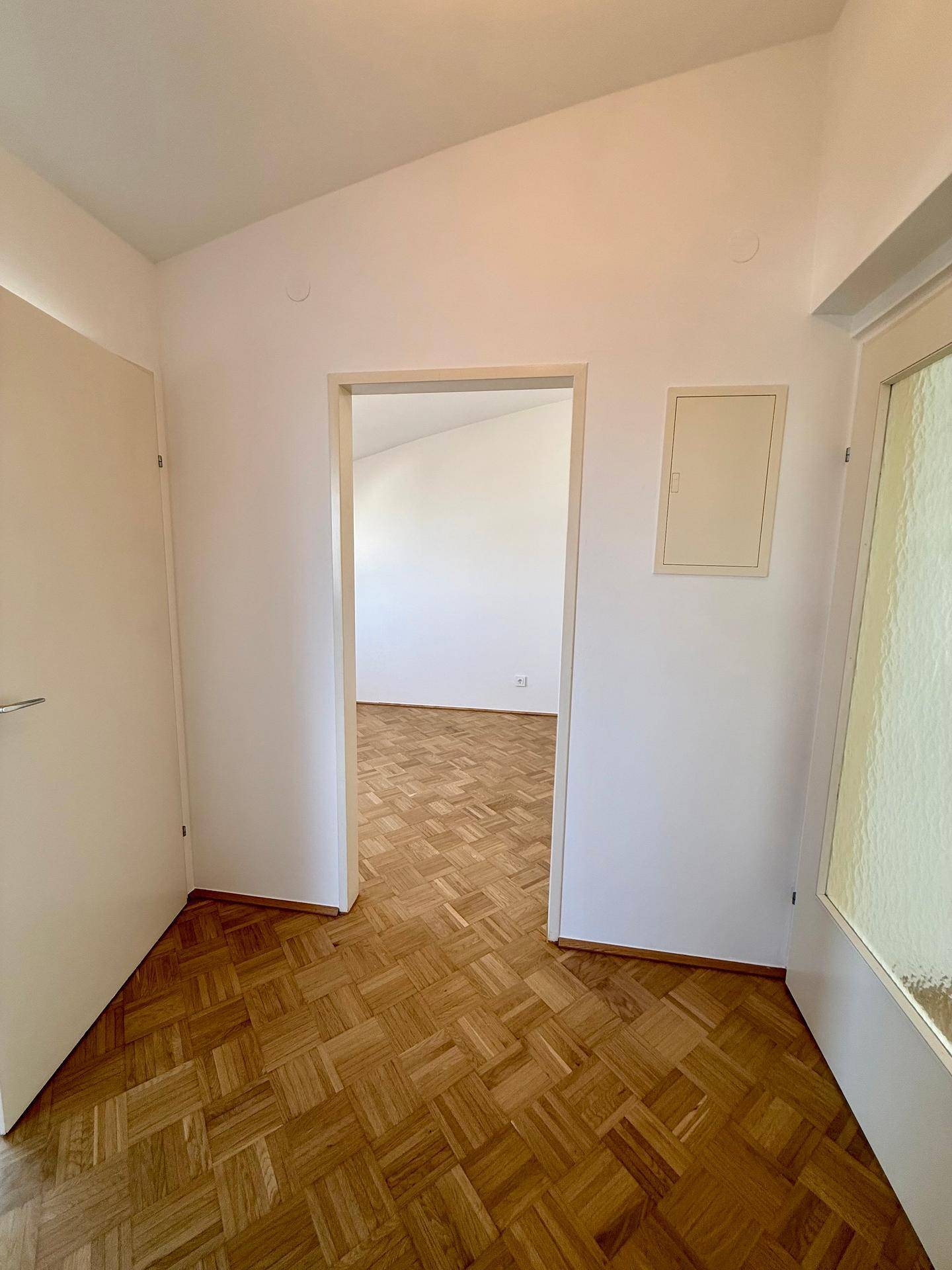 Heller Flur mit Parkettboden, der zu einem weiteren Zimmer mit Dachschrägen führt.