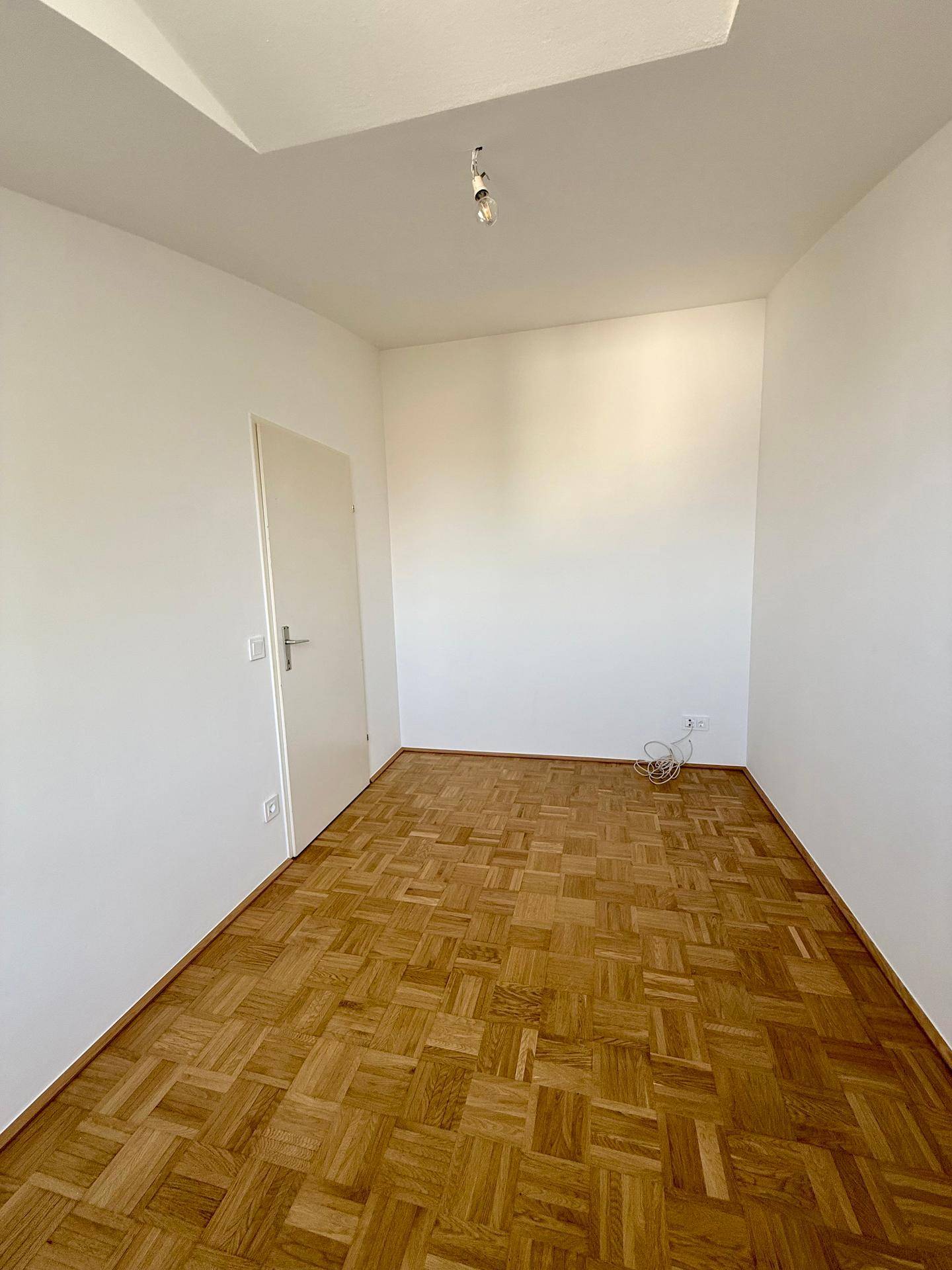 Geräumiges Schlafzimmer mit Parkettboden und weiß gestrichenen Wänden, ideal für ein Kinderzimmer.