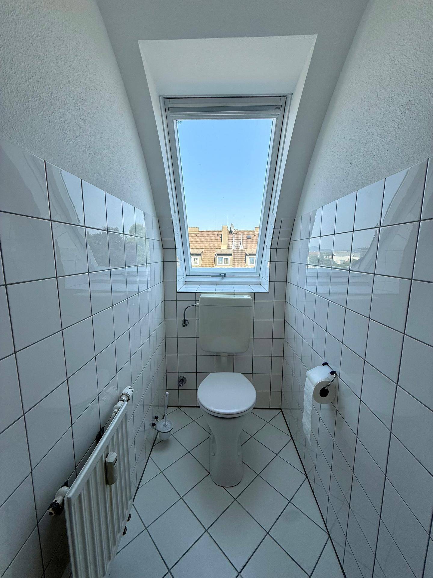 Separate Toilette mit Dachfenster, weißen Fliesen und Heizkörper, bietet Tageslicht.