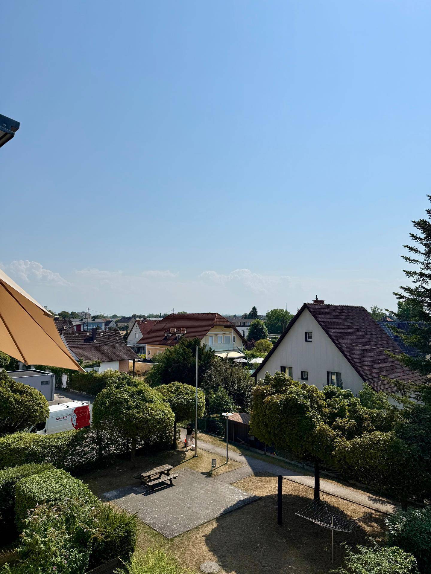 Ausblick vom Balkon auf eine grüne Umgebung mit Bäumen und Wohnhäusern.