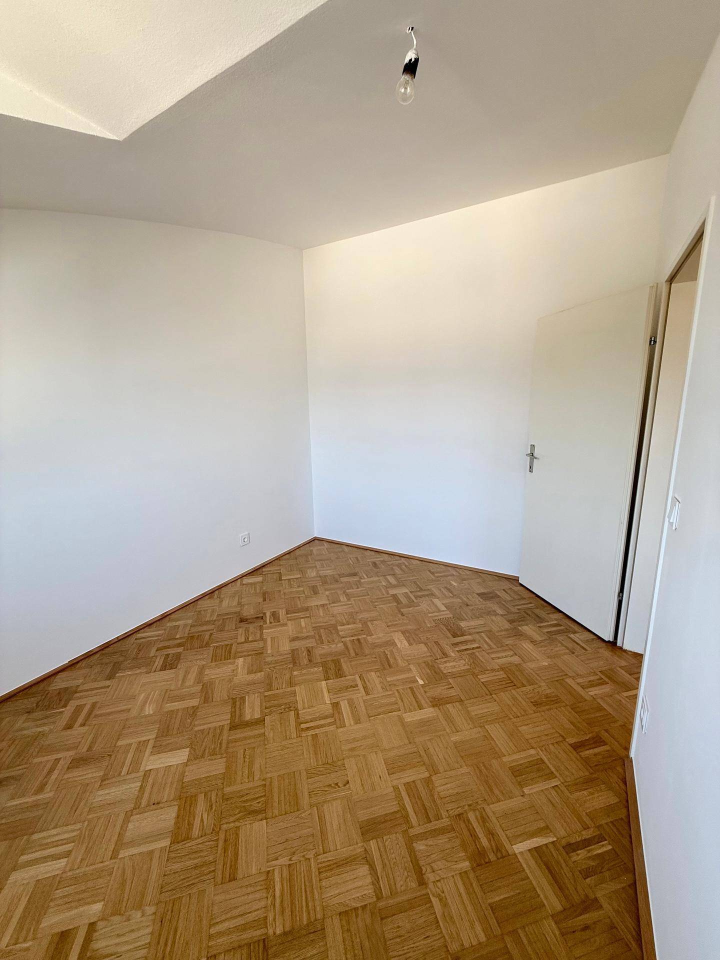 Leeres Schlafzimmer mit Parkettboden und weiß gestrichenen Wänden, bereit zur Einrichtung.