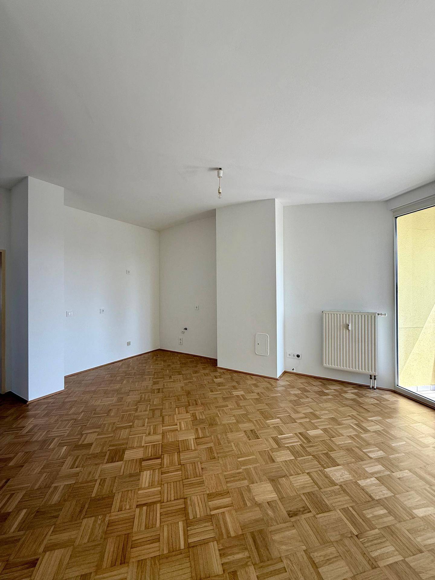 Leeres Wohnzimmer mit Parkettboden und Heizkörpern, bereit für individuelle Gestaltung.