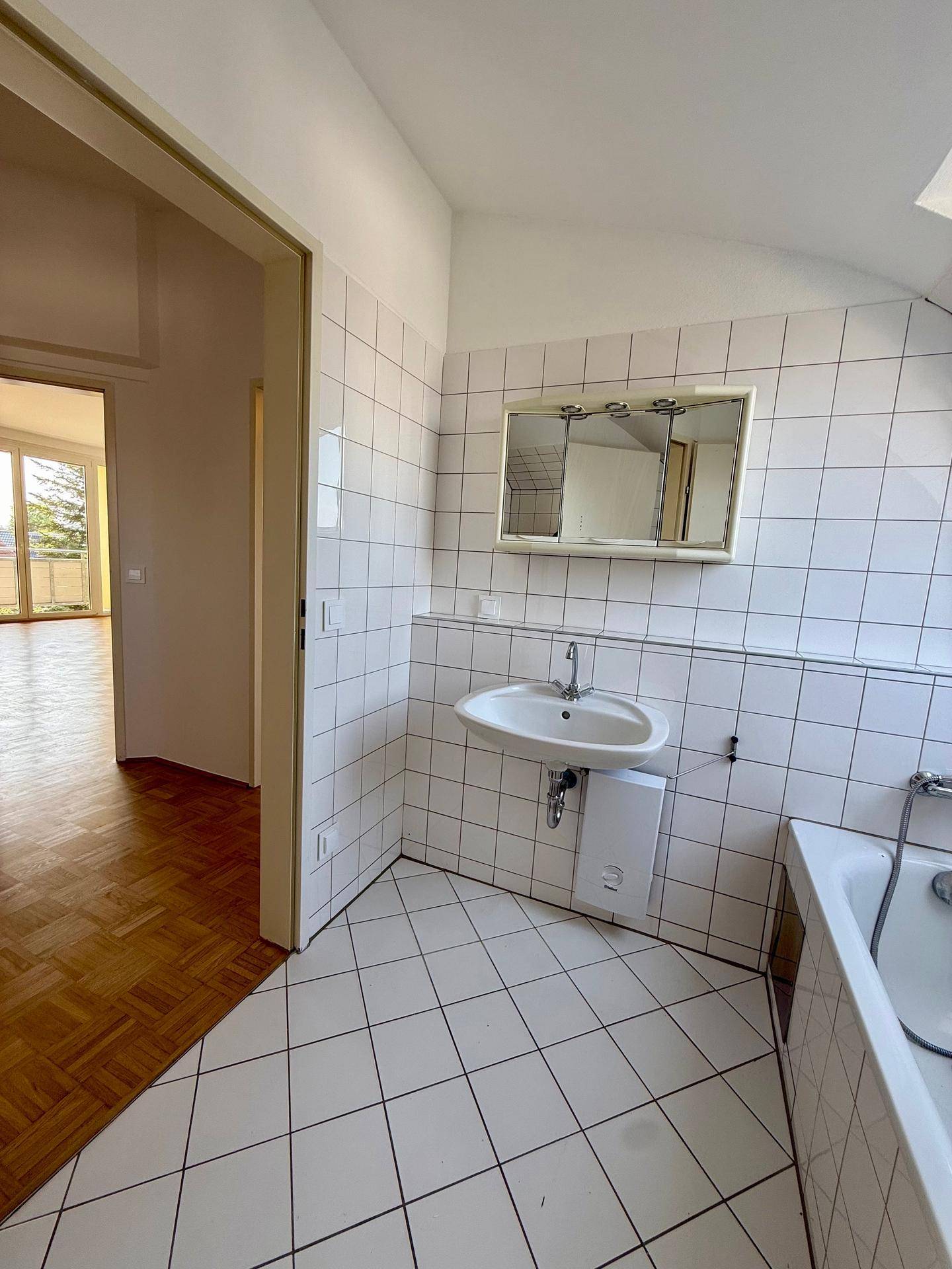 Helles Badezimmer mit Waschbecken, Spiegelschrank und Badewanne, gefliest in Weiß.