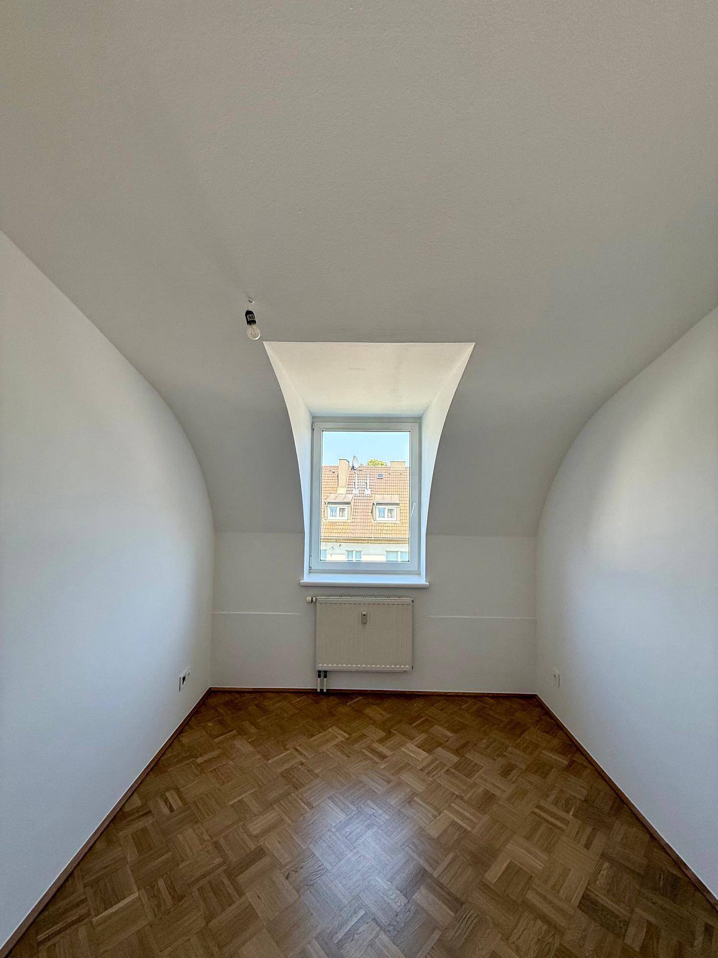 Schlafzimmer mit Parkettboden, Dachschräge und einem Fenster, das viel Licht spendet.