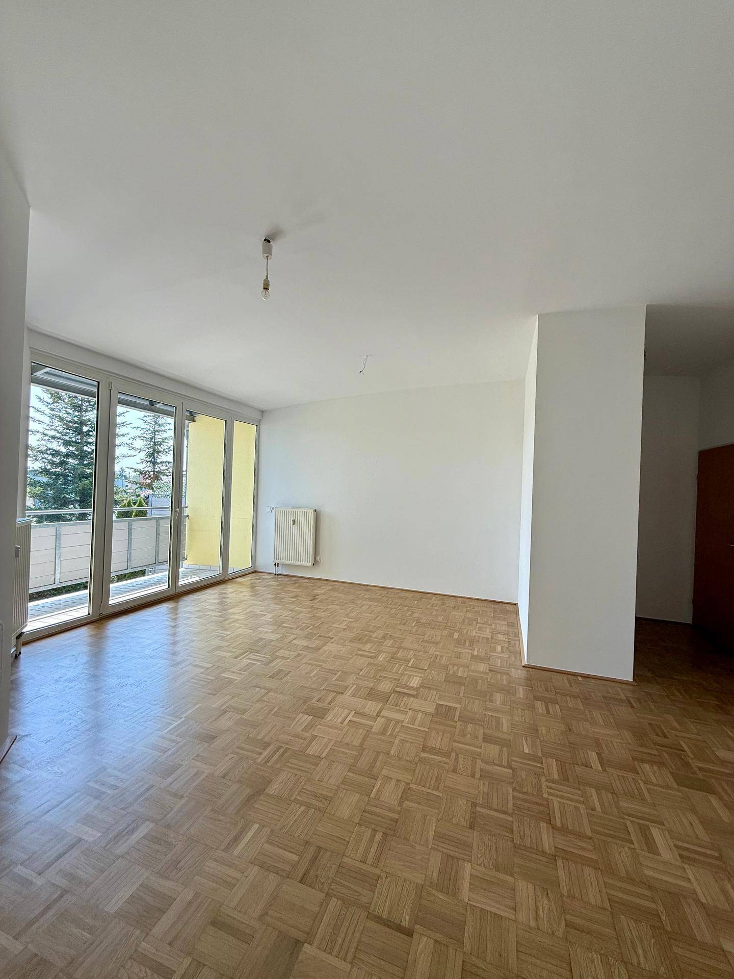 Geräumiges Wohnzimmer mit Parkettboden und großen Fenstern, die viel Sonnenlicht hereinlassen.