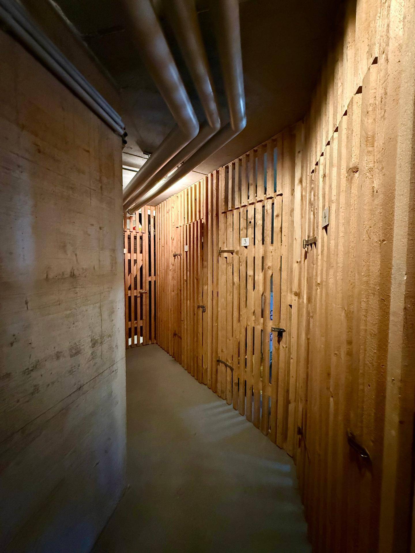 Kellerabteile mit Holzlattenwänden und Betonboden, bieten individuellen Stauraum.