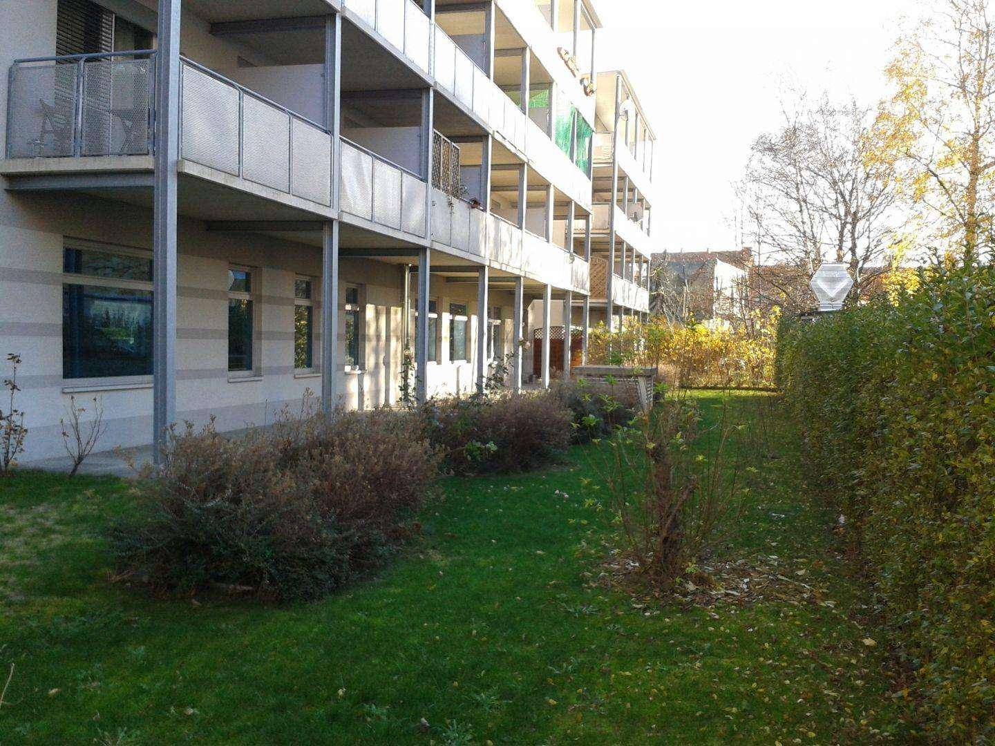 Mehrstöckiges Gebäude mit Balkonen und einer gepflegten Rasenfläche mit Hecken im Vordergrund.