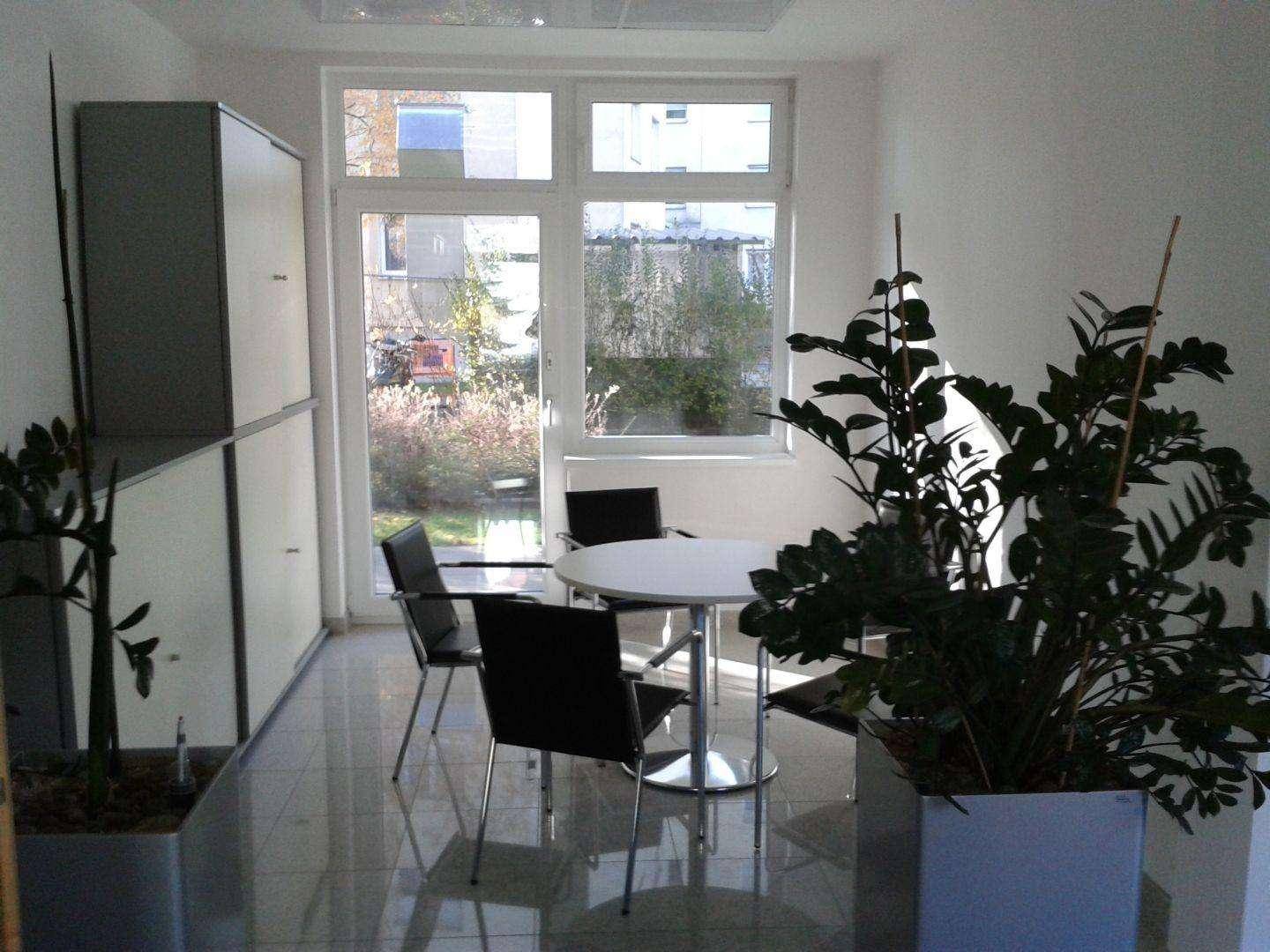 Kleiner Besprechungsraum mit rundem Tisch, Stühlen und Pflanzen, hell durch ein großes Fenster.