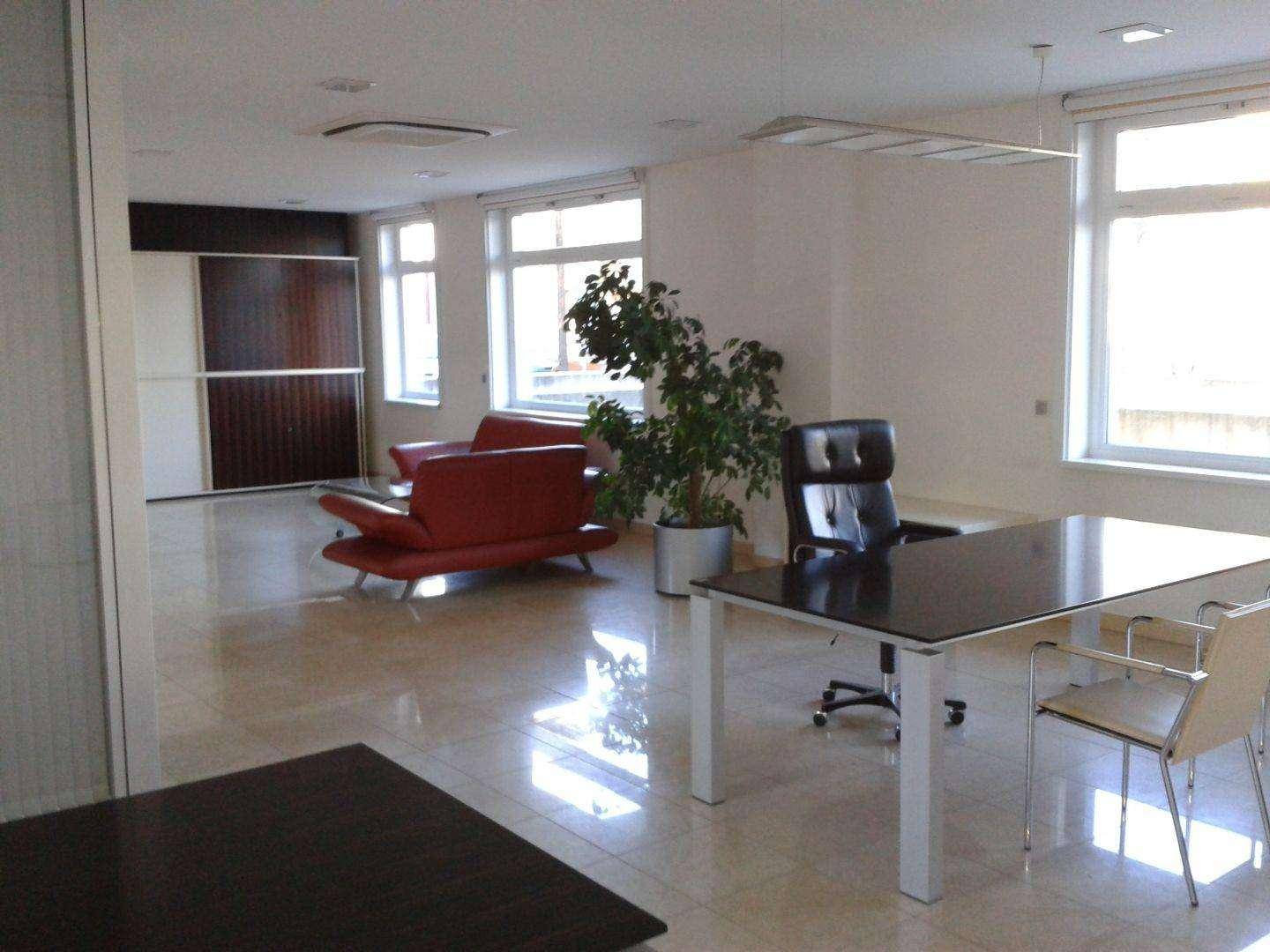 Heller Büroraum mit rotem Sofa, Schreibtisch und großen Fenstern, die viel Tageslicht hereinlassen.