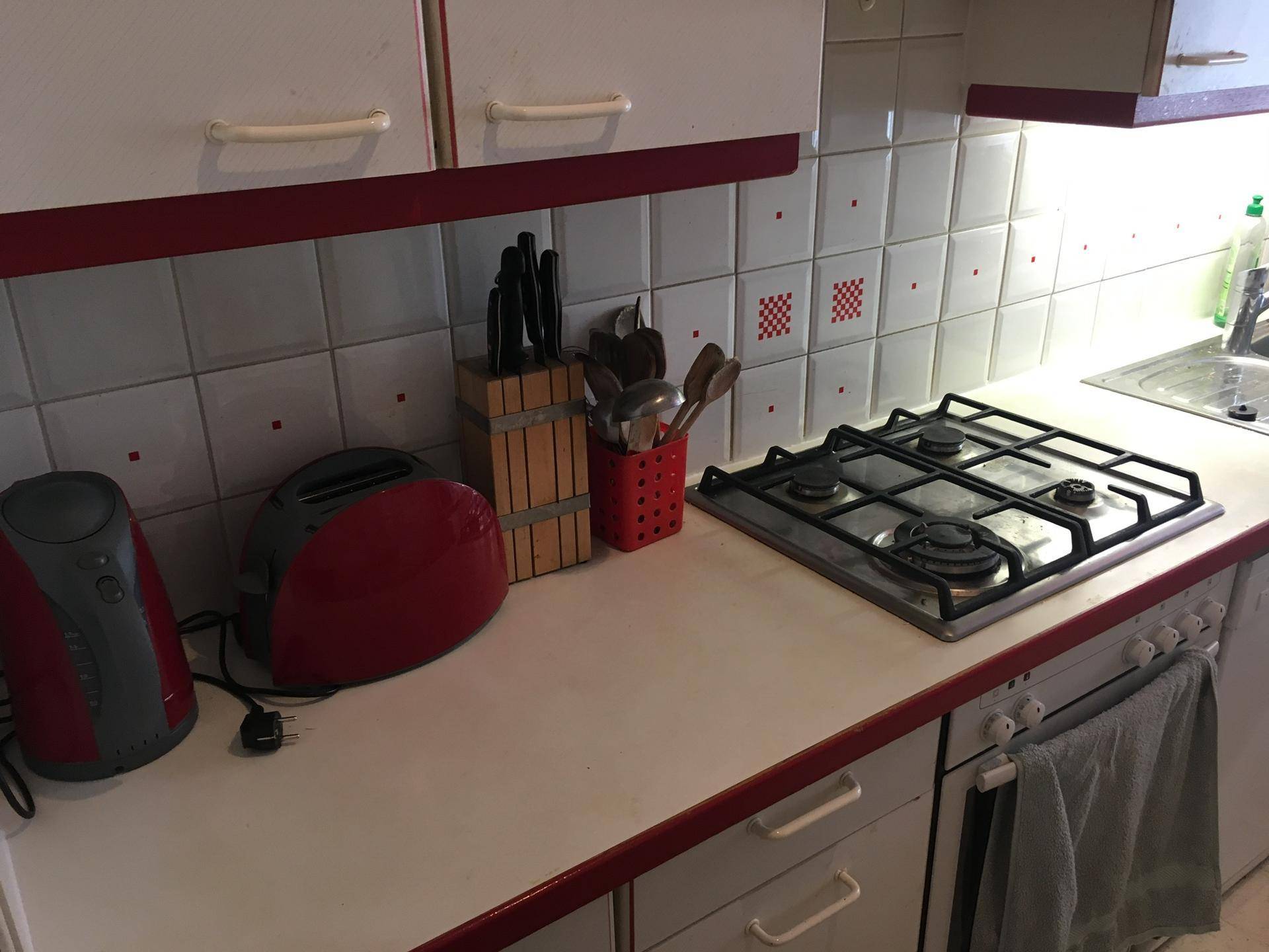 Küche mit Gasherd, Spüle, roten Akzenten und weißen Fliesen als Spritzschutz über der Arbeitsplatte.